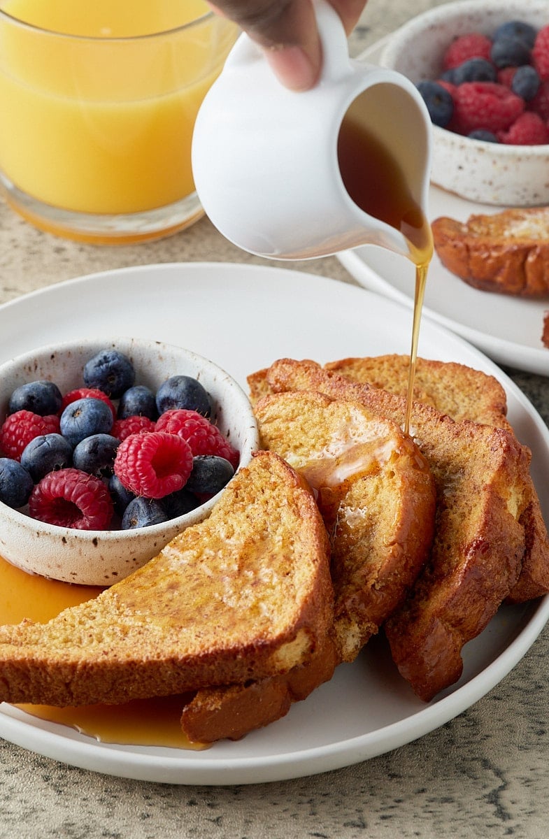 Maple syrup being poured from a white jug over air fryer French toast.