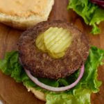 A cooked hamburger pattu on a bun topped with pickles.