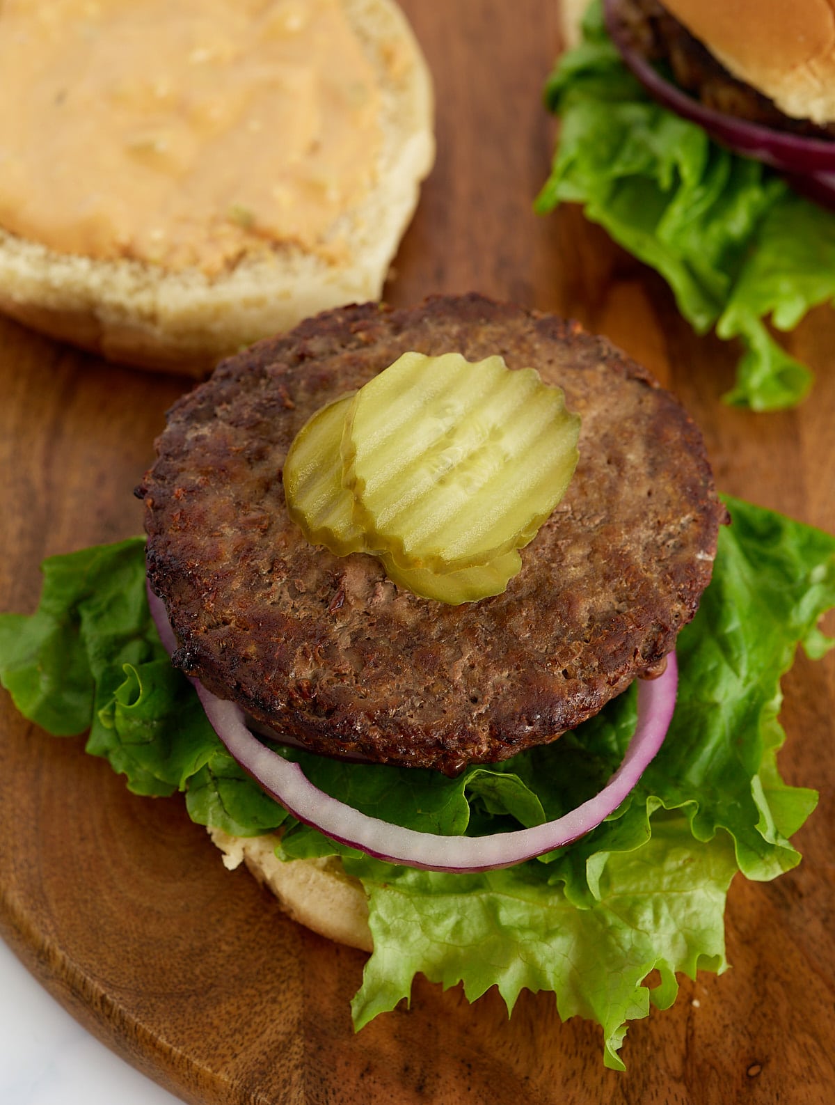 A cooked hamburger pattu on a bun topped with pickles.