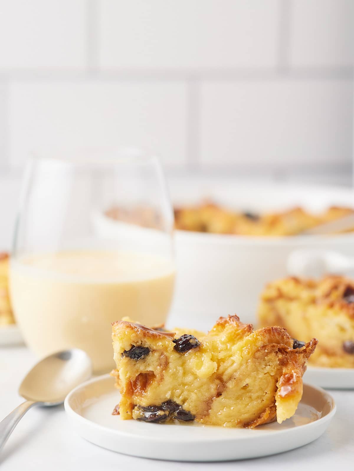 A slice of bread pudding served next to a glass of eggnog.