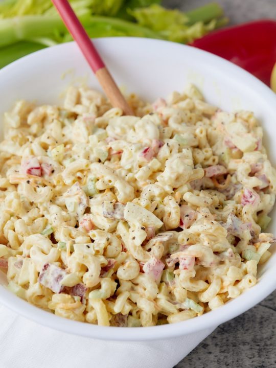 A spoon in a bowl of creamy macaroni salad.