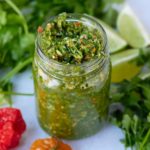 green seasoning in glass jar with herbs surrounding it