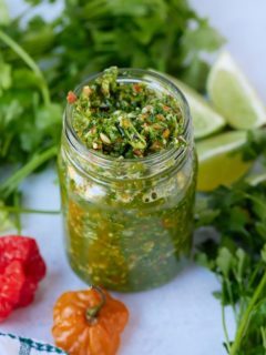 green seasoning in glass jar with herbs surrounding it