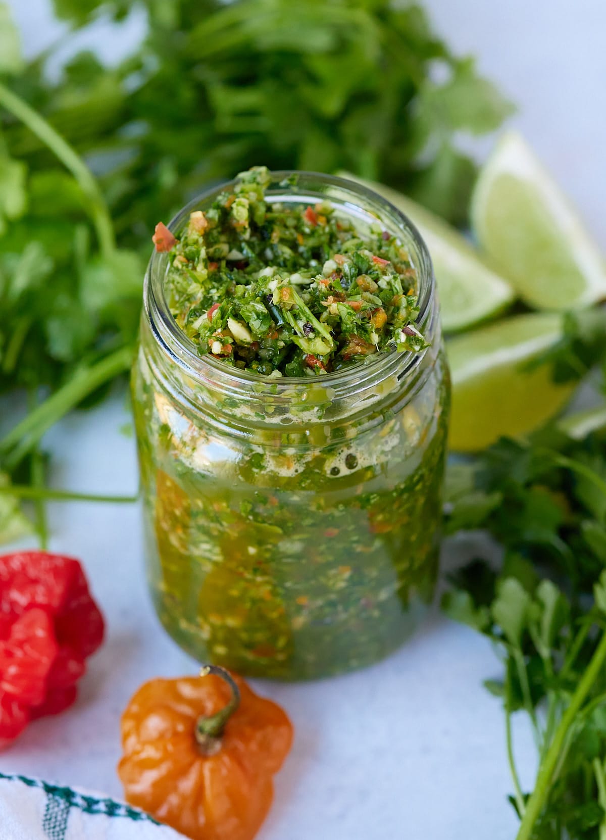 green seasoning in glass jar with herbs surrounding it
