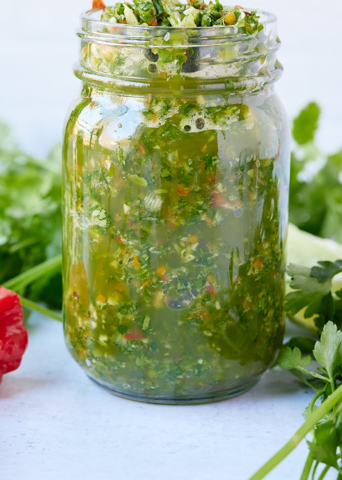 green seasoning in glass jar with herbs surrounding it