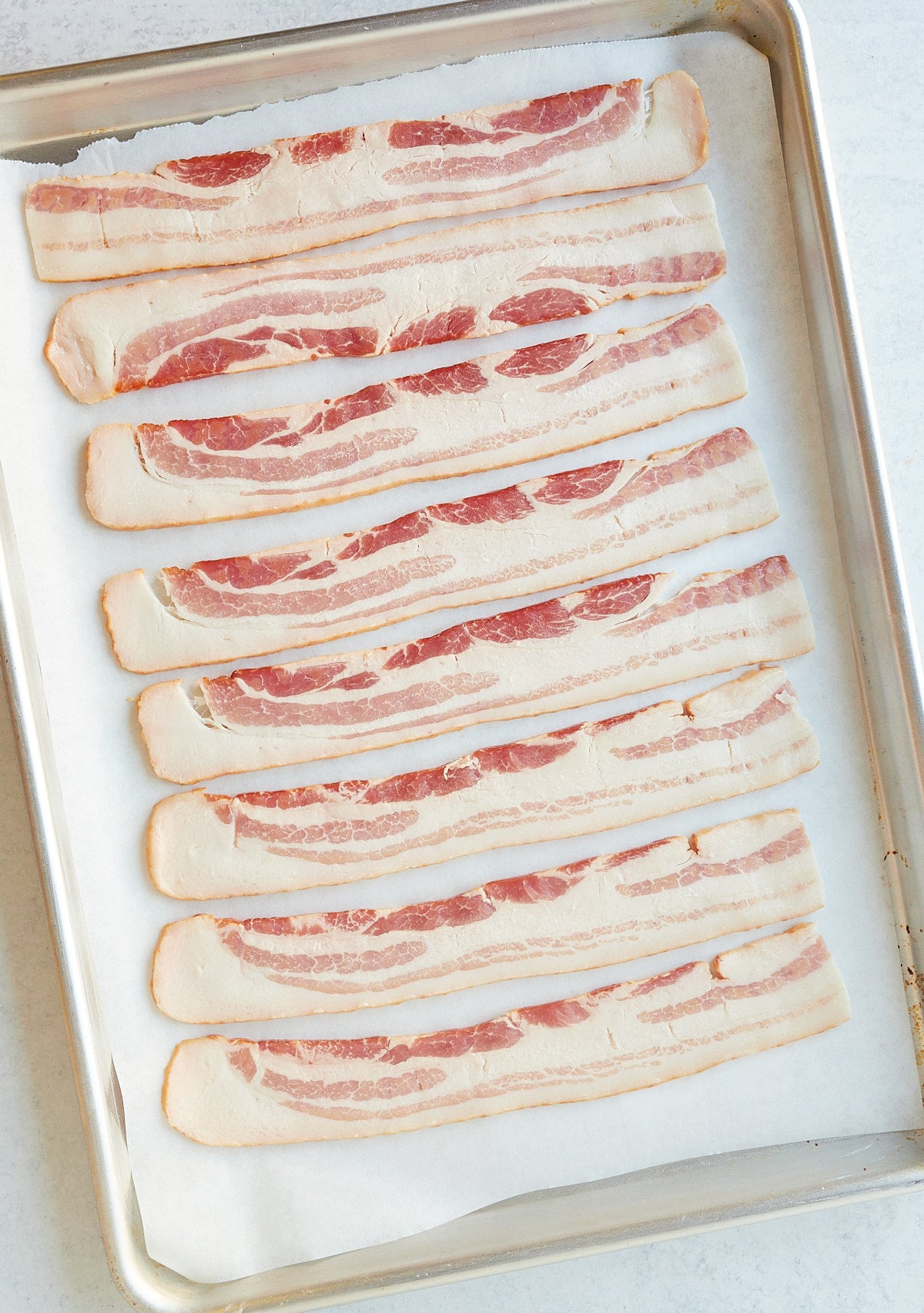 Strips of bacon on a lined baking sheet before being cooked.