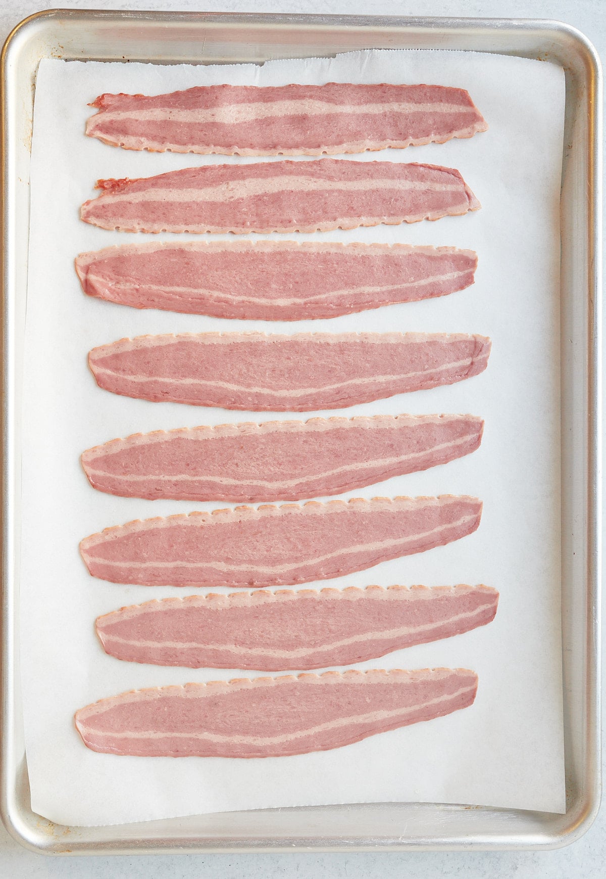 Strips of turkey bacon on a lined baking sheet before being cooked.
