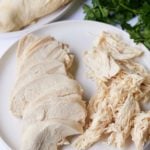 cooked chicken breast on white plate sliced and shredded with parsley on the side