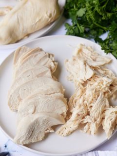 cooked chicken breast on white plate sliced and shredded with parsley on the side