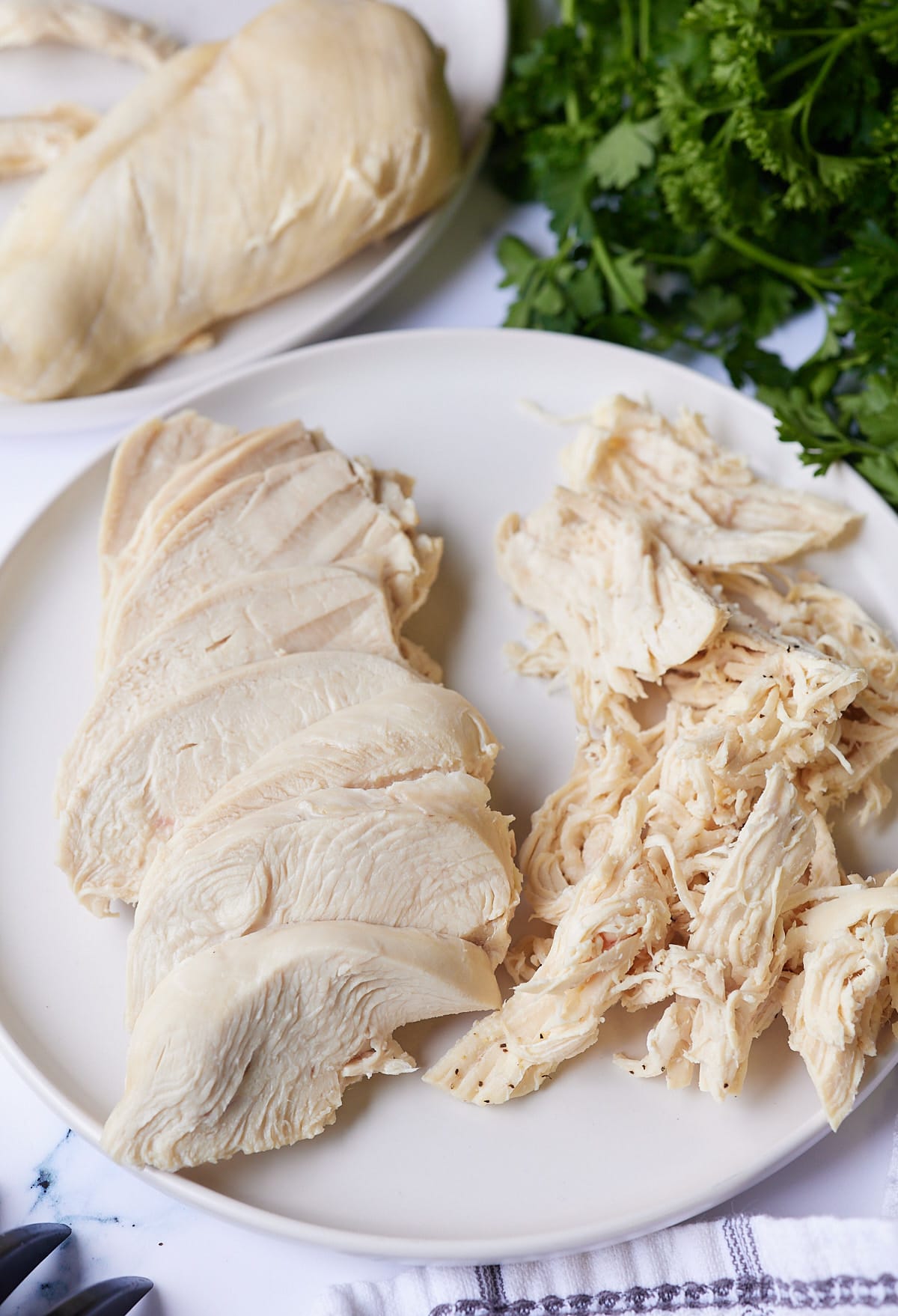 cooked chicken breast on white plate sliced and shredded with parsley on the side