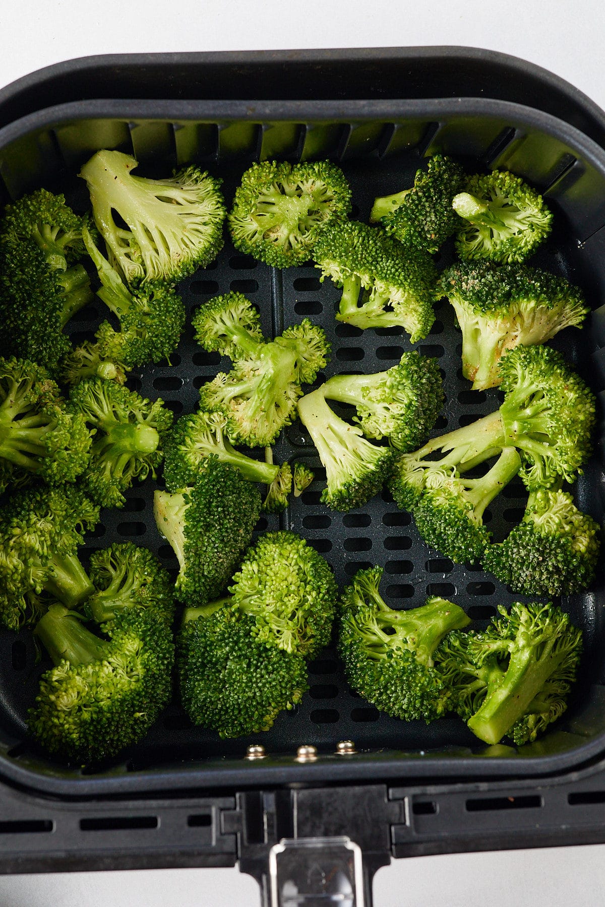 Raw broccoli in an air fryer basket.