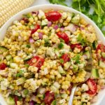 A fresh corn salad served in a white bowl with a spoon.