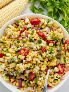 A fresh corn salad served in a white bowl with a spoon.