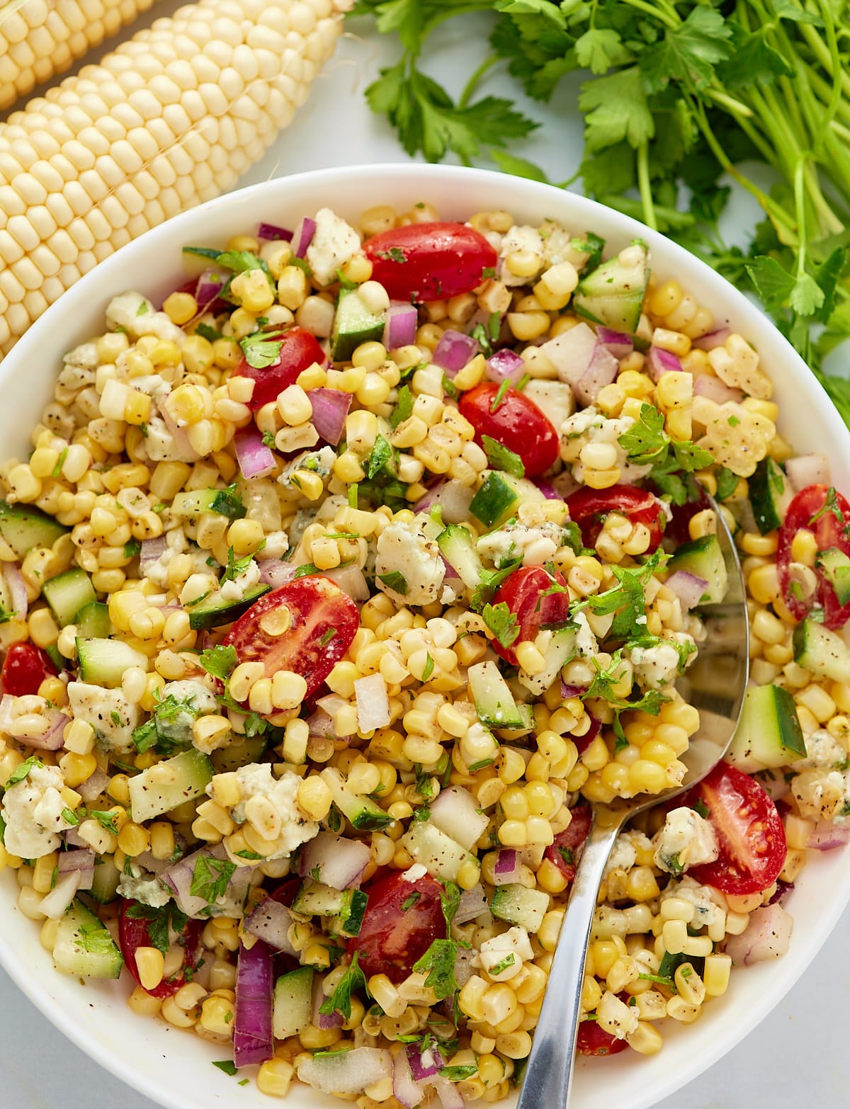 A fresh corn salad served in a white bowl with a spoon.