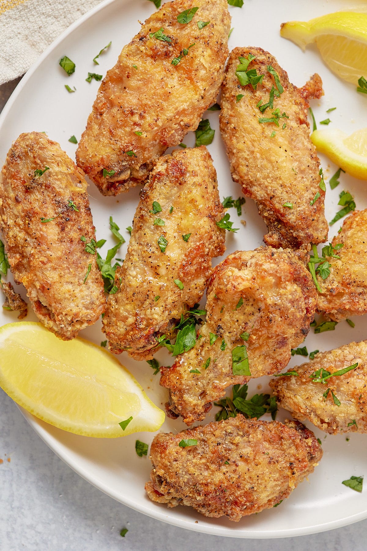 Air fried chicken wings on a white plate with lemon wedges.