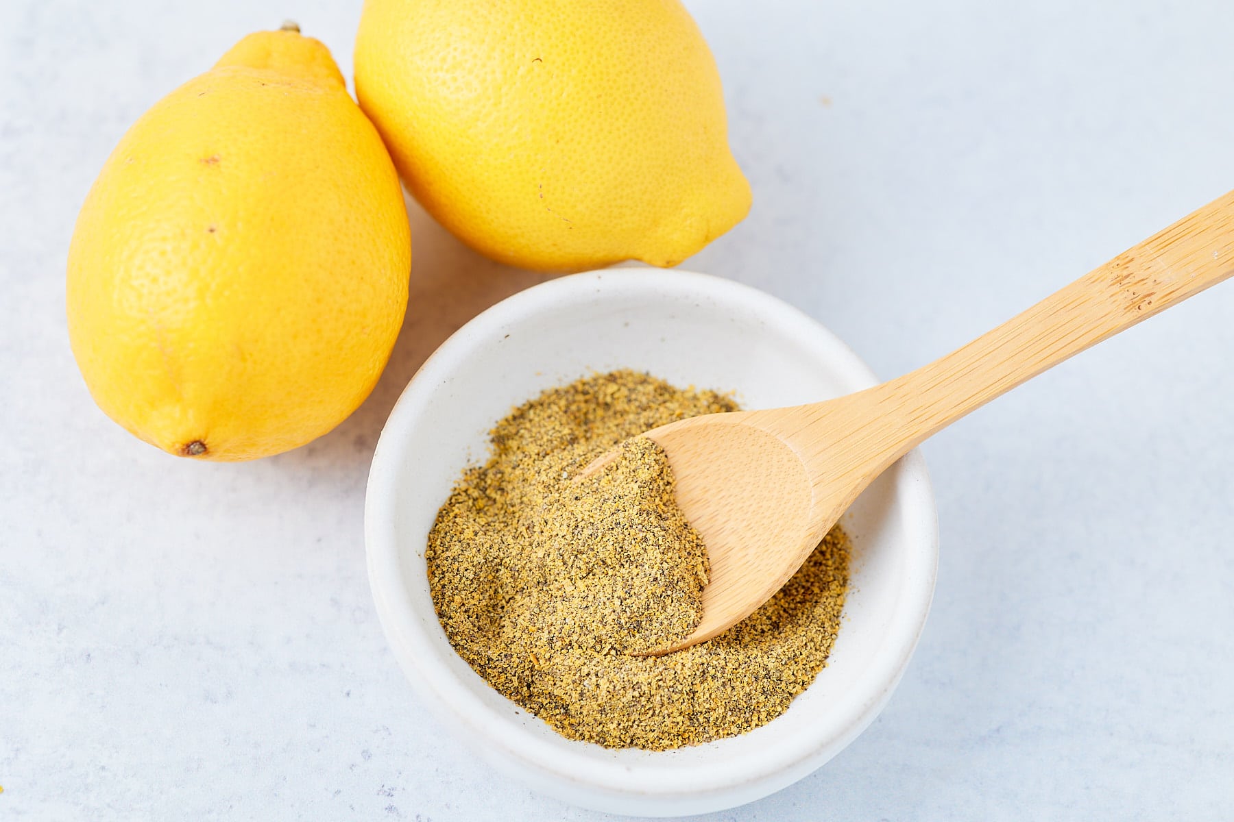 Lemon pepper seasoning in a bowl next to fresh lemons.