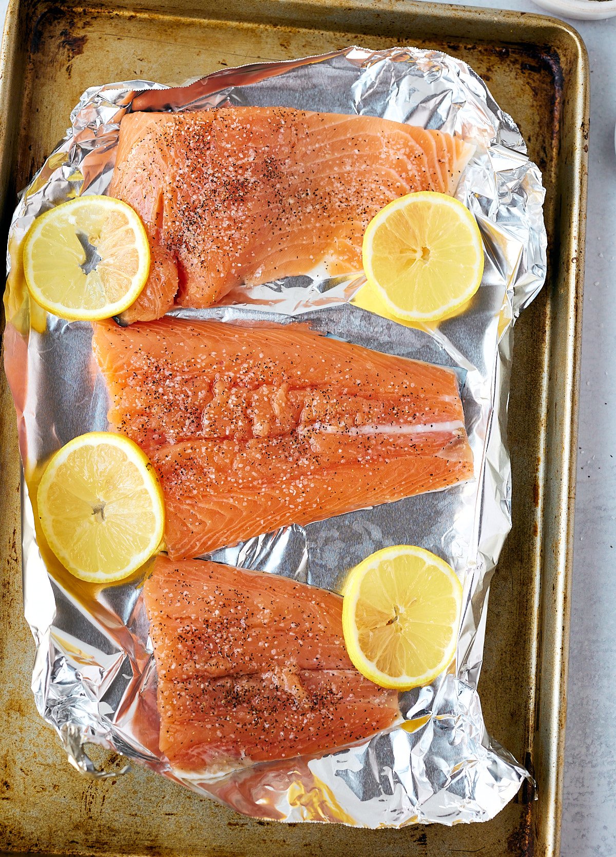 Salmon fillets on a lined baking sheet with slices of lemon.