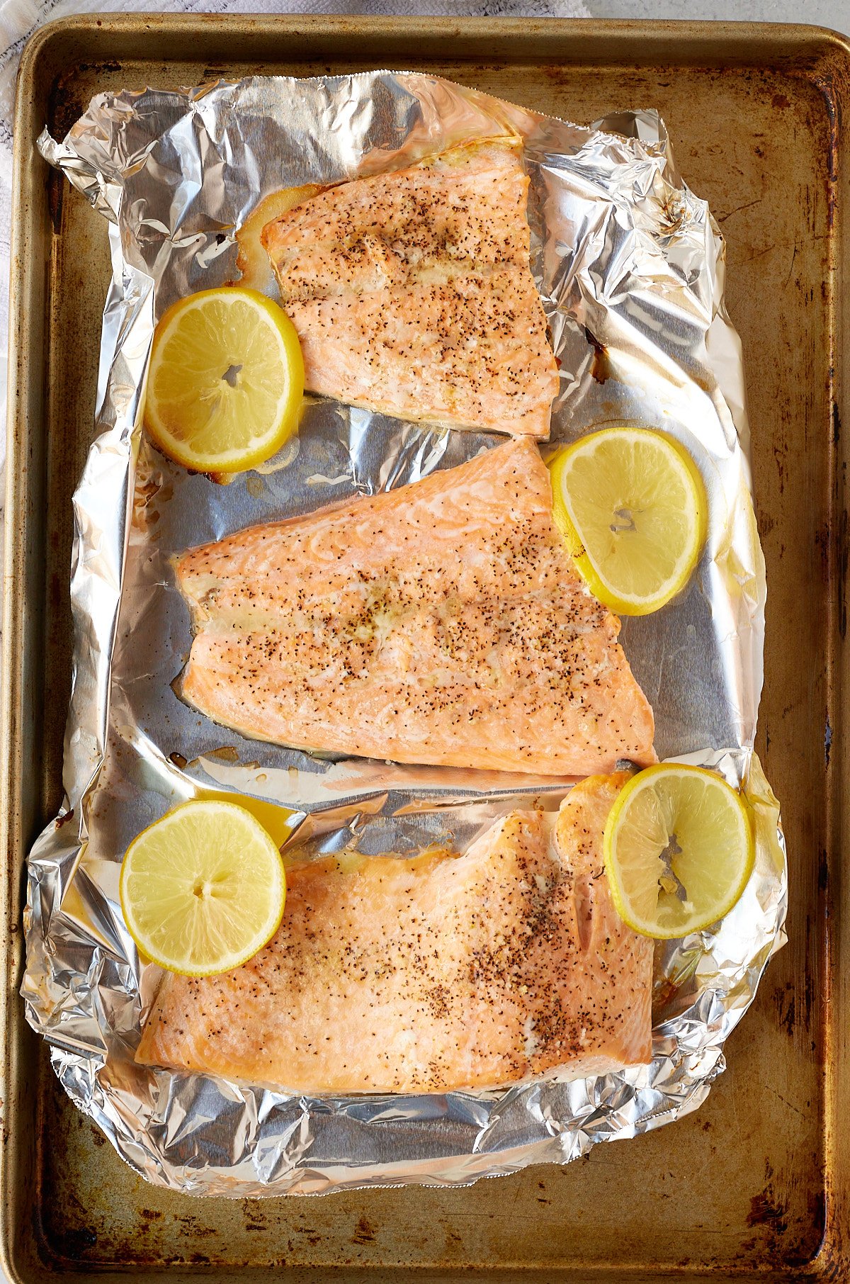 Oven baked salmon fillets on a lined baking tray.