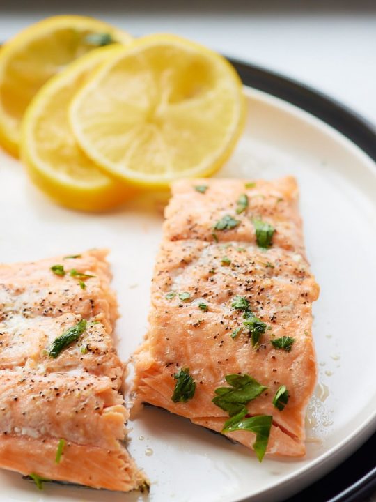 Oven baked salmon fillets on a plate with slices of lemon.
