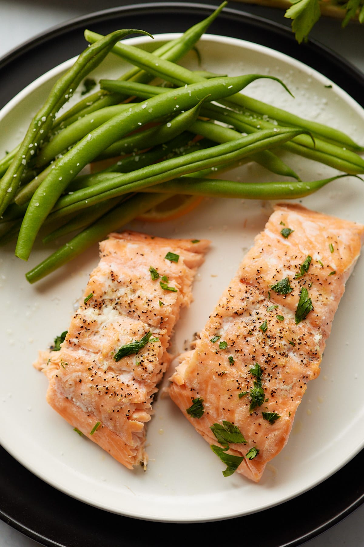 Overhead shot of salmon fillets served on a white plate with green beans.