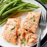 Two salmon fillets on a plate with green beans. One fillet cut in half.