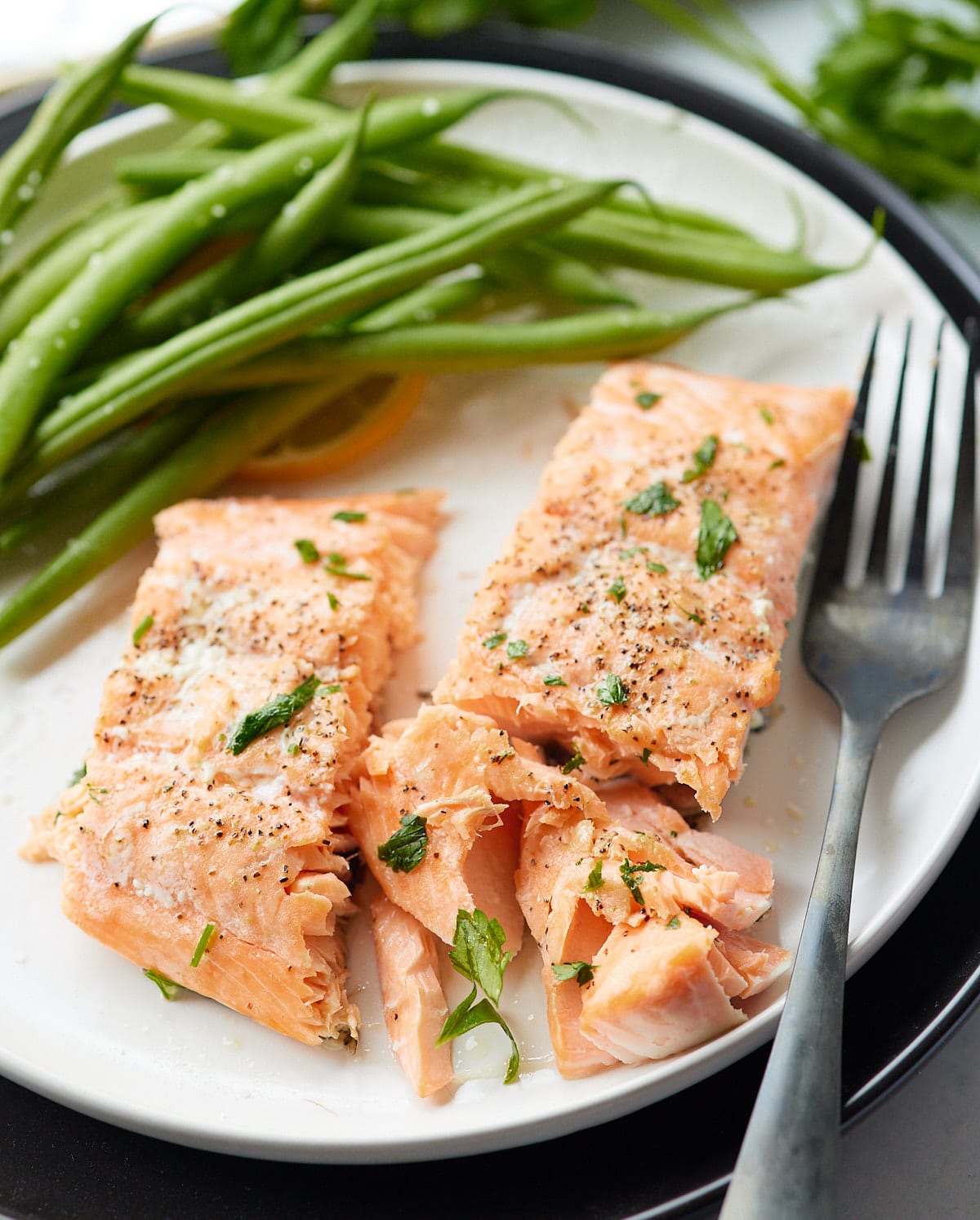 Two salmon fillets on a plate with green beans. One fillet cut in half.
