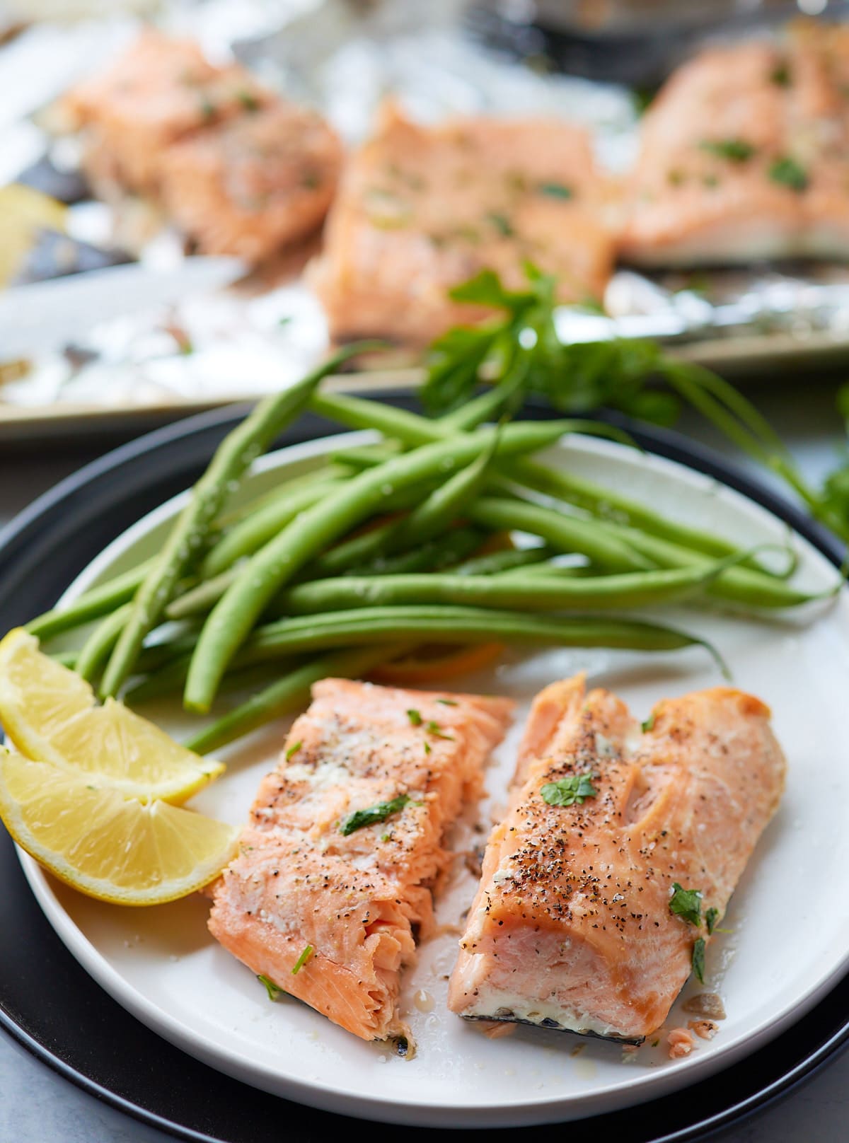 Two salmon fillets served with green beans and a lemon wedge.