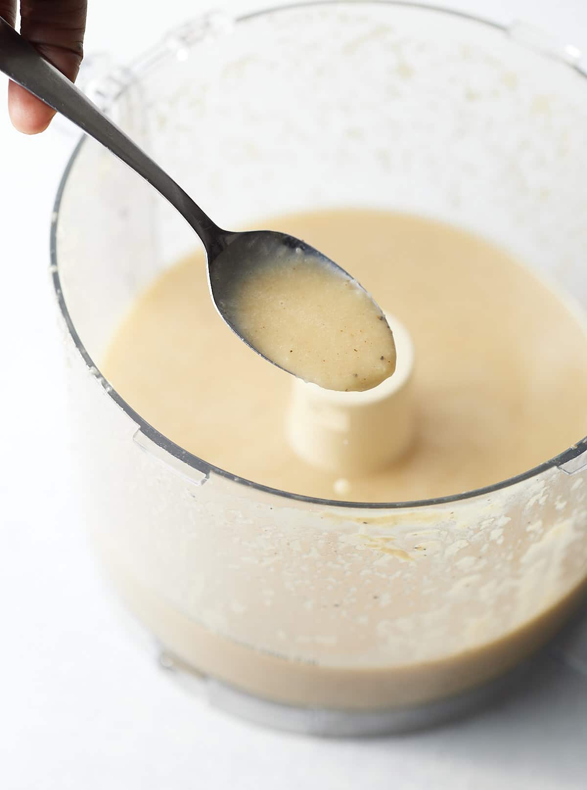 The dressing on a spoon over a food processor.