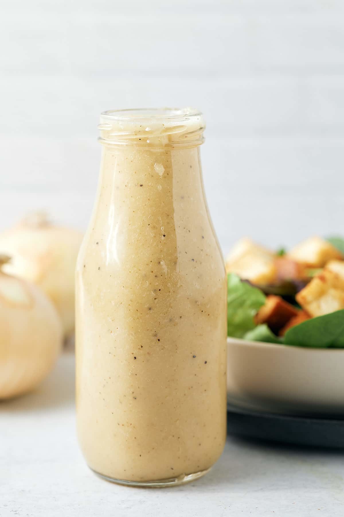 Sweet onion dressing in a glass bottle next to a fresh salad bowl.