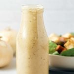 Sweet onion dressing in a glass bottle next to a fresh salad bowl.
