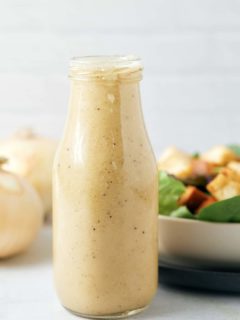 Sweet onion dressing in a glass bottle next to a fresh salad bowl.