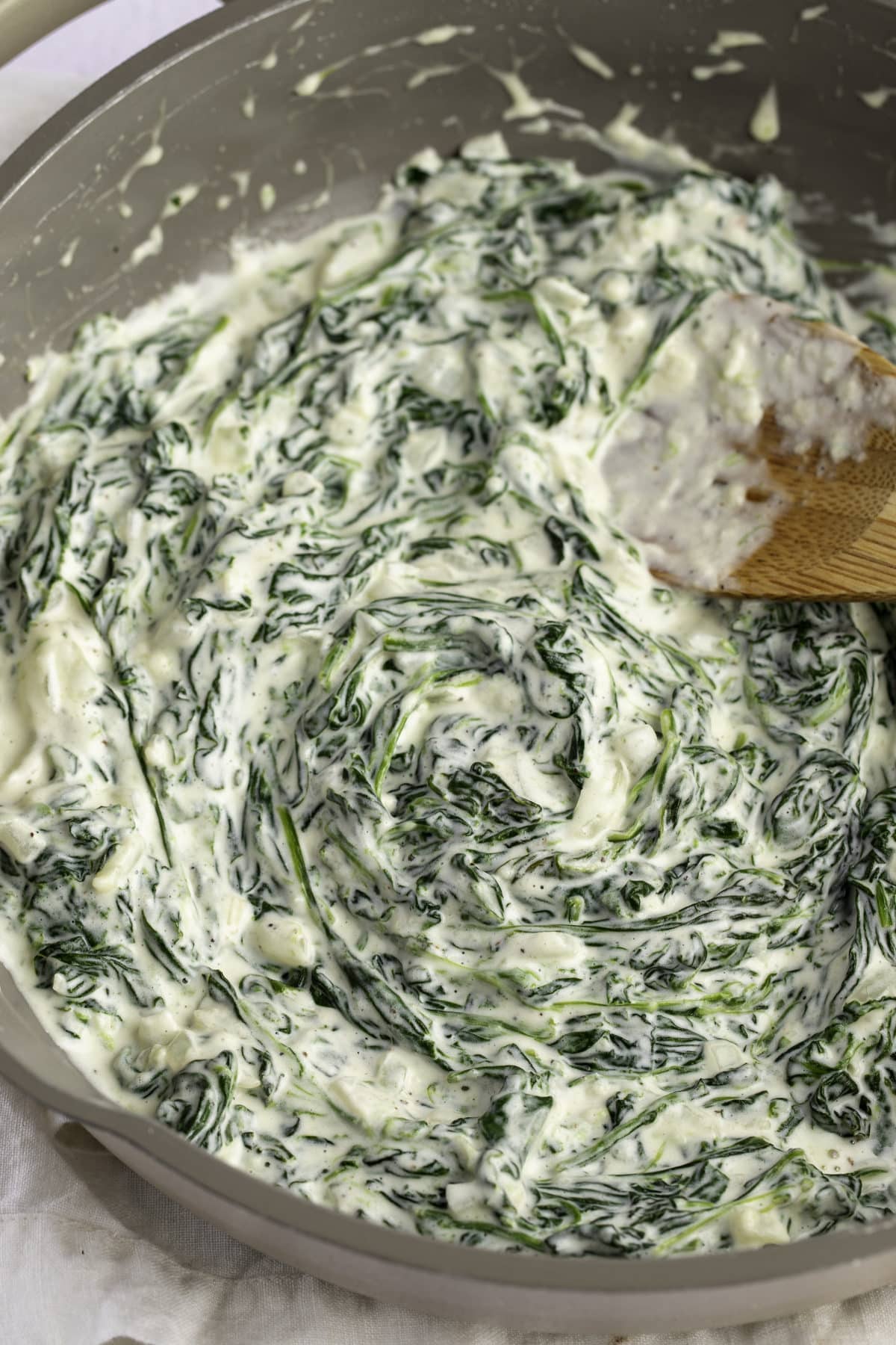 A wooden spoon stirring the steakhouse creamed spinach.