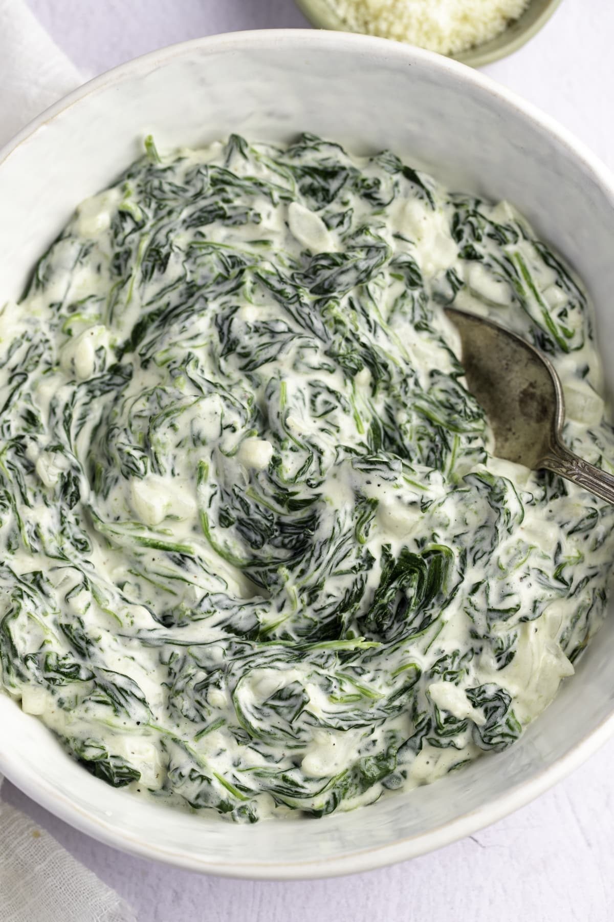 Thick creamed spinach in a white serving bowl with a spoon.