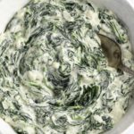 Thick creamed spinach in a white serving bowl with a spoon.