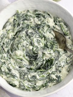 Thick creamed spinach in a white serving bowl with a spoon.