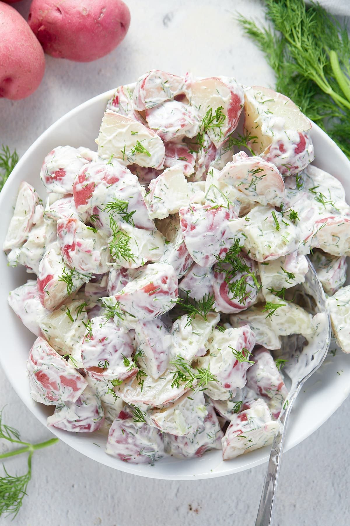 Overhead shot of creamy dill potato salad in a white serving bowl.