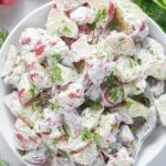 Overhead shot of creamy dill potato salad in a white serving bowl.