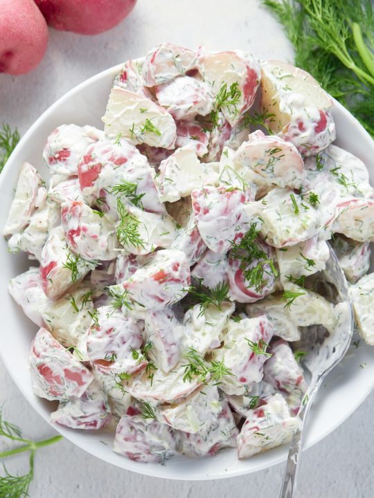 Overhead shot of creamy dill potato salad in a white serving bowl.