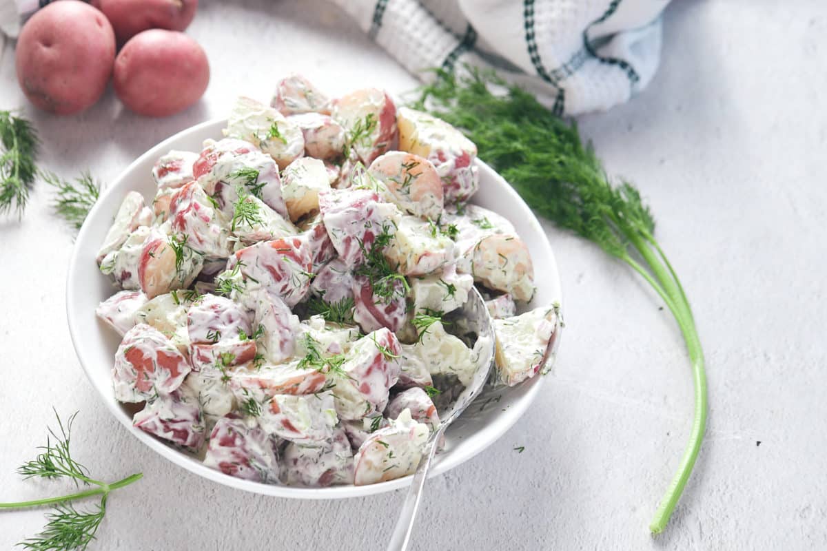 A bowl of potato salad next to a piece of fresh dill.