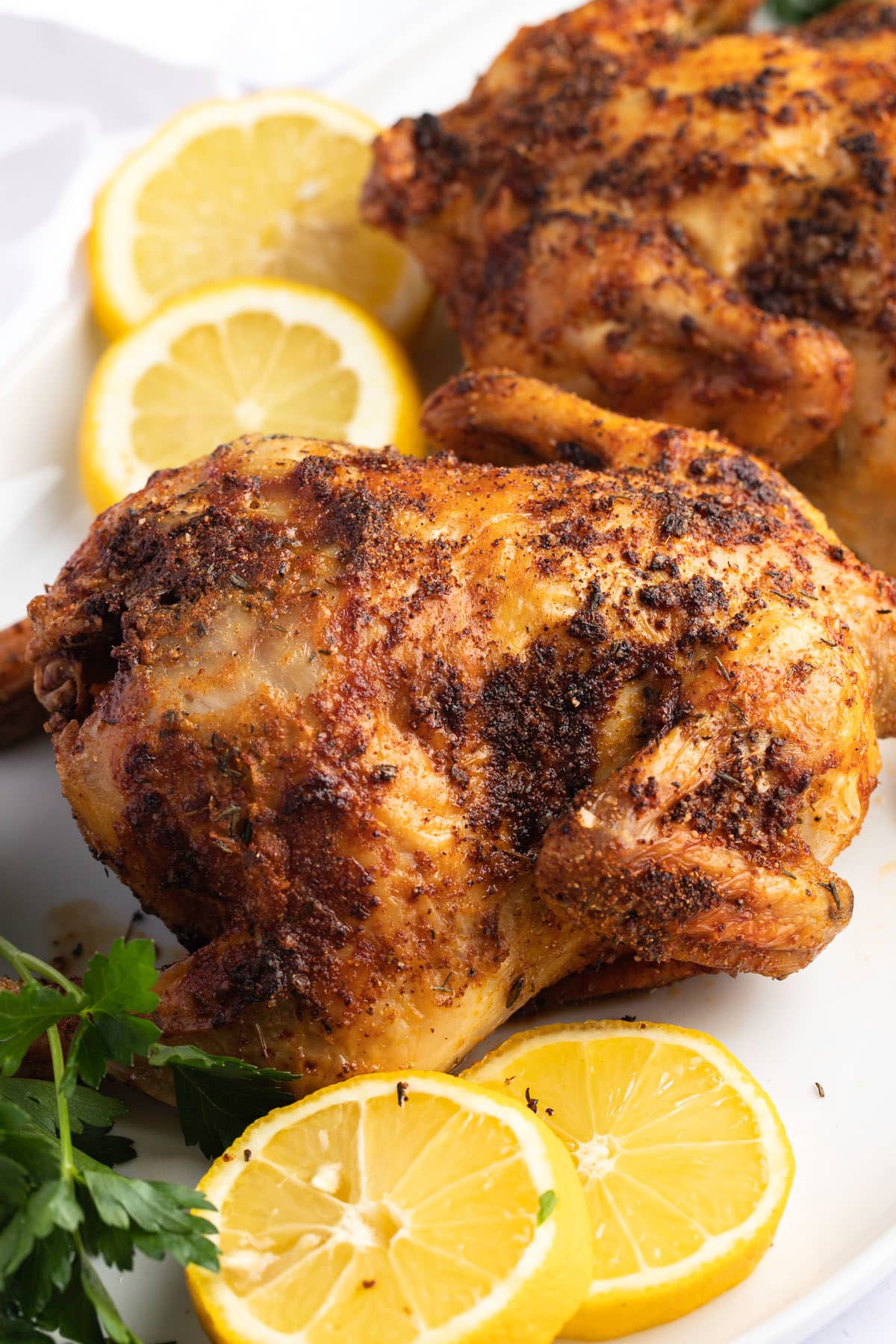 An air fryer cornish hen served with slices of lemon.