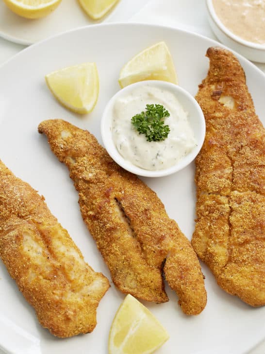 air fryer fish on white plate with tatar sauce and lemons