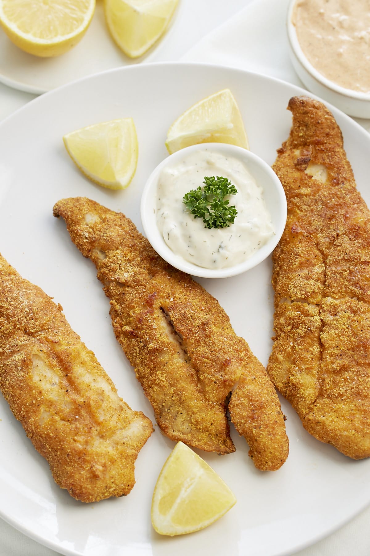 air fryer fish on white plate with tatar sauce and lemons