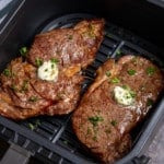 two steaks in the air fryer basket with garlic butter on top