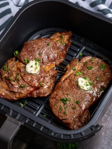 two steaks in the air fryer basket with garlic butter on top