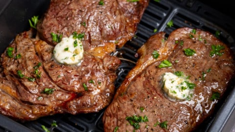 two steaks in the air fryer basket with garlic butter on top