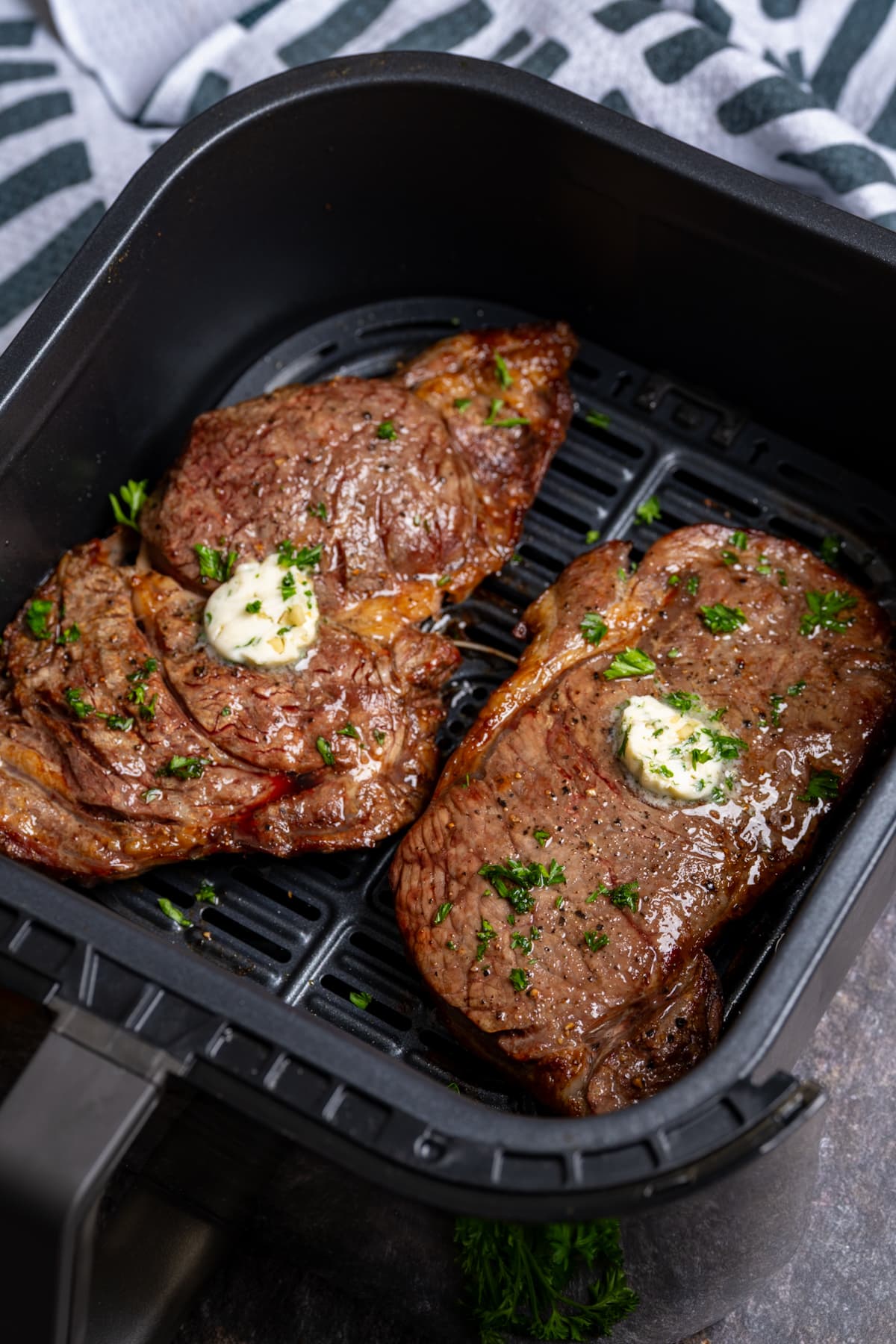 two steaks in the air fryer basket with garlic butter on top