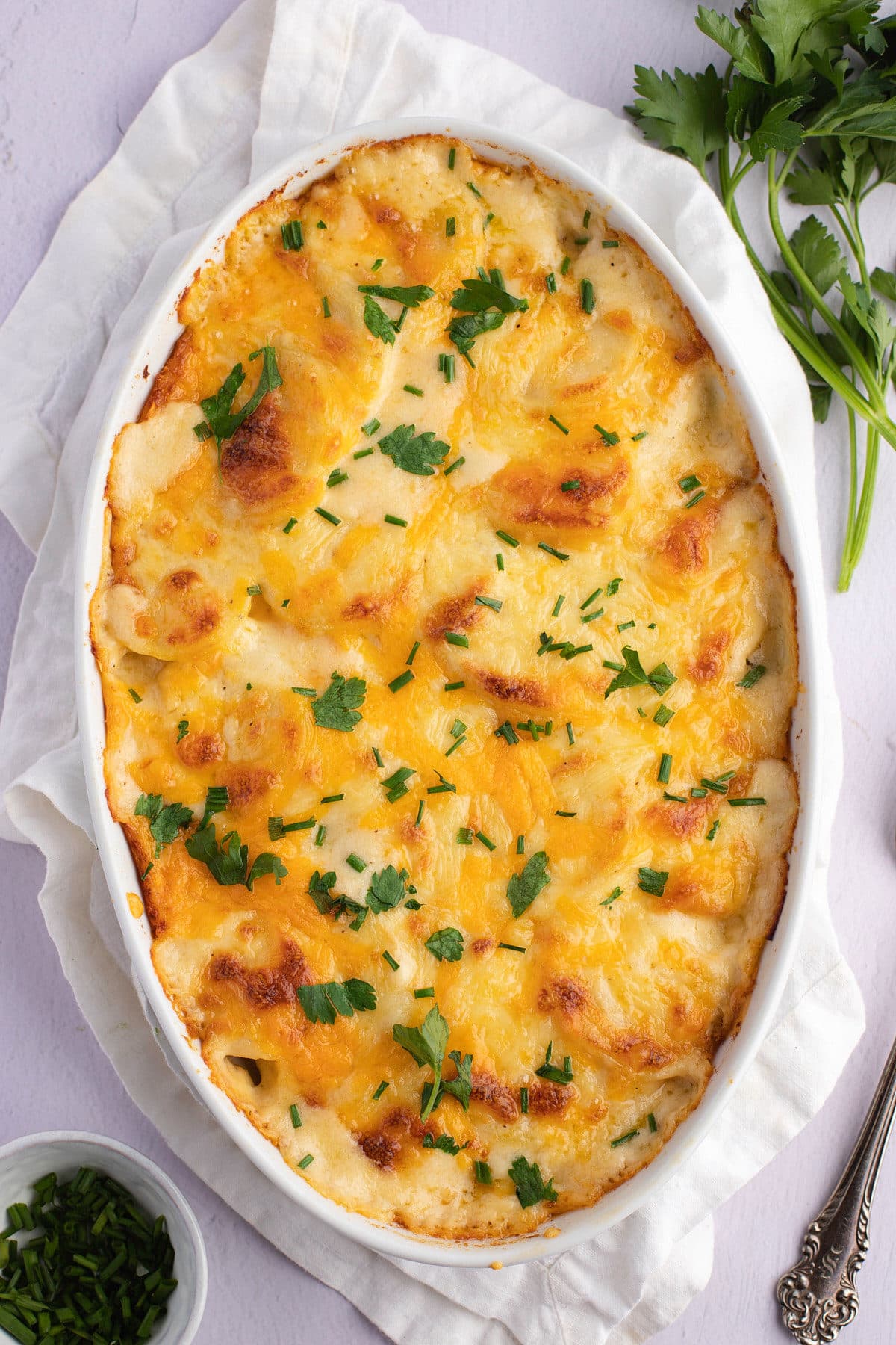 Cheesy scalloped potatoes in a white dish garnished with fresh herbs.