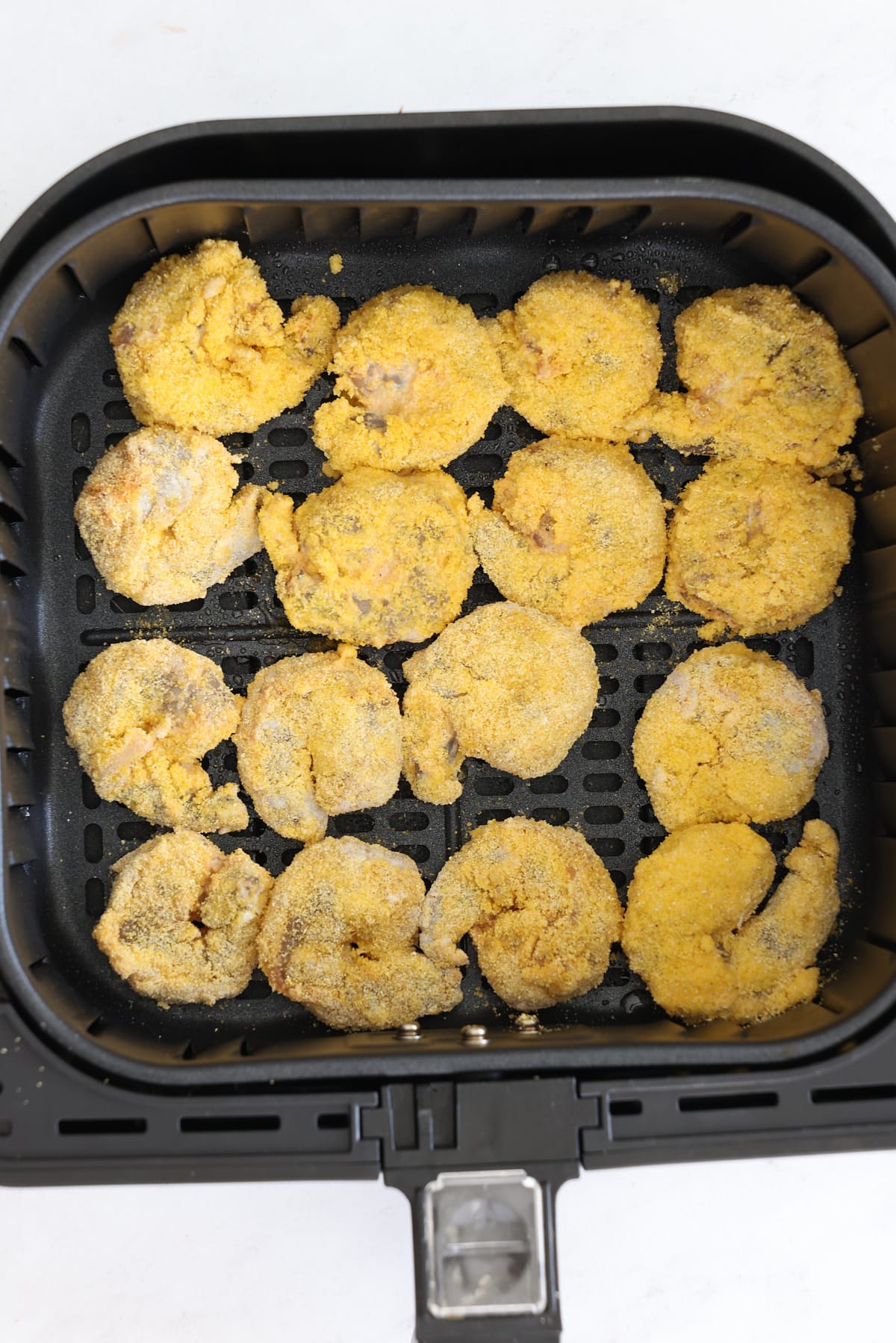 The dredged shrimp in an air fryer basket.