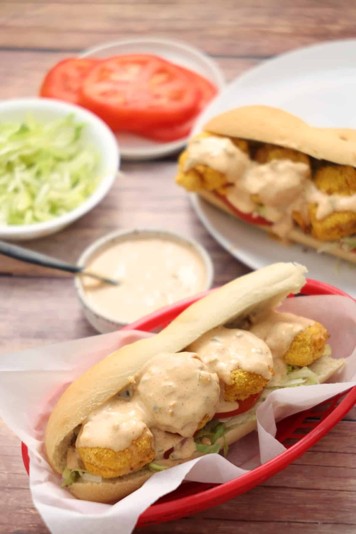 Air fryer po'boy shrimp sandwiches next to bowls and plates with the sandwich sauce and toppings.