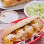 Two air fryer shrimp po'boy sandwiches in red serving baskets lined with parchment.